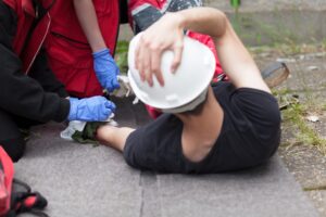 A worker with a white hardhat lays injured on the ground.