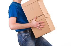 A man in a blue t-shirt carrying 2 cardboard boxes. 