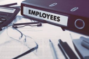 A binder with the word 'employees' on, on a table with paper and glasses. 