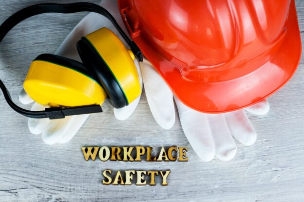 A hard hat and safety gloves next to wooden letters that spell 'workplace safety'.